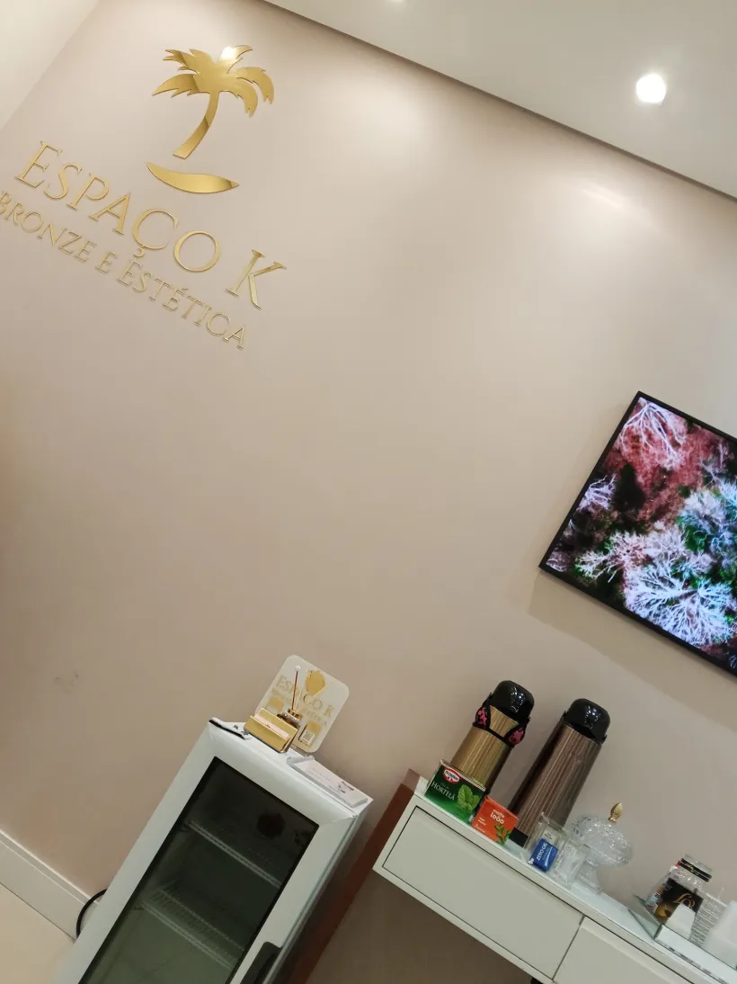 Logo dourado do Espaço K na parede, com cantinho do café