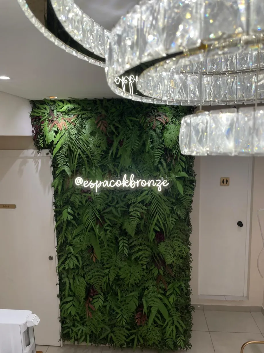 Recepção do Espaço K Bronze e Estética, com parede de plantas e lustre de cristal